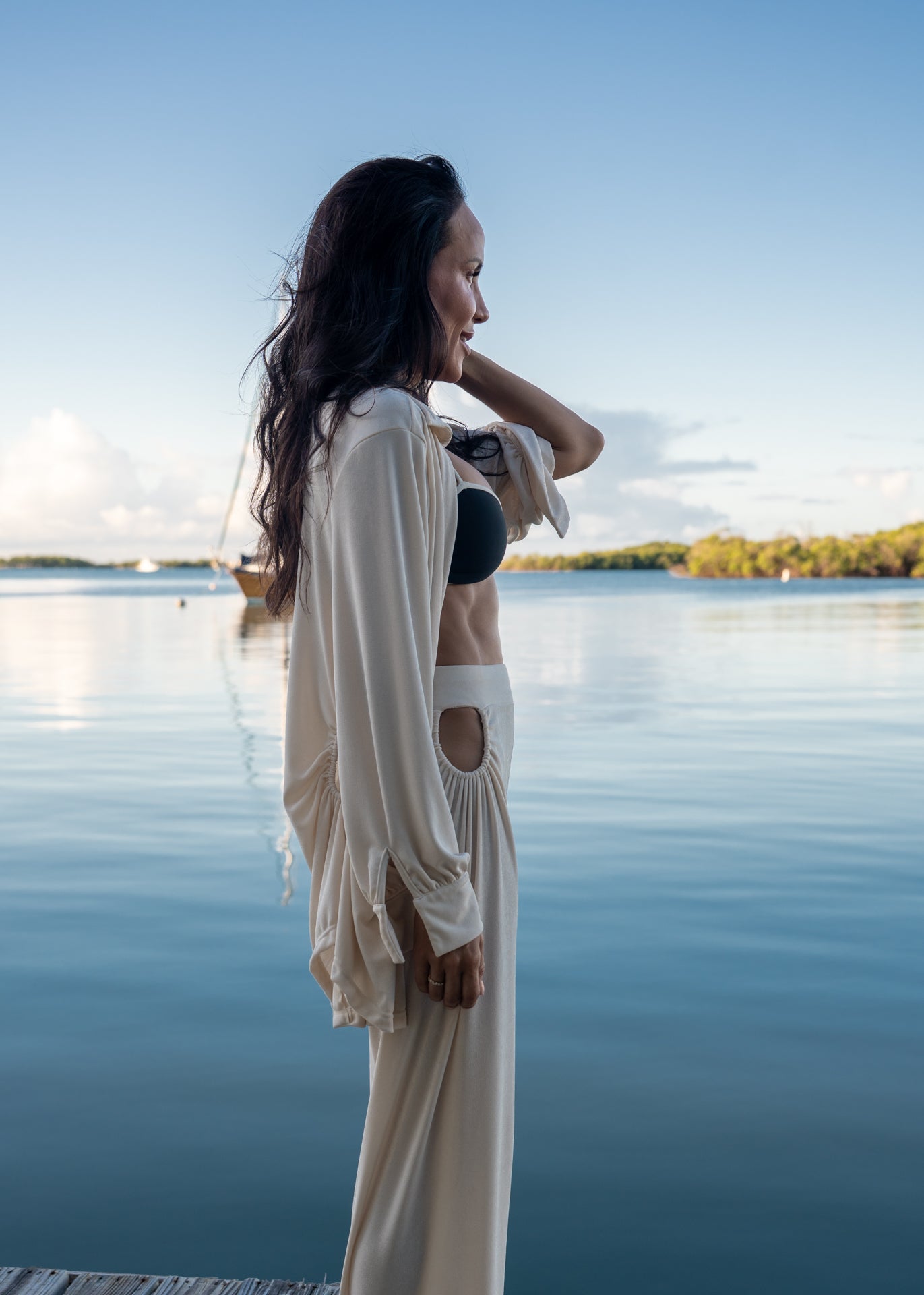 Woman standing by a lake wearing a white outfit with cut-out details.